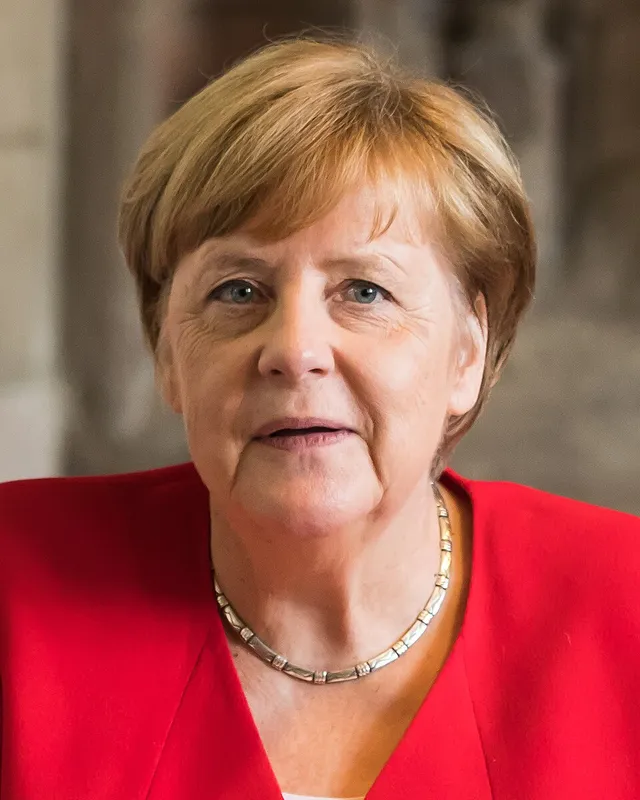 Photograph of Angela Merkel in 2019, in a coloured blazer, facing the camera.