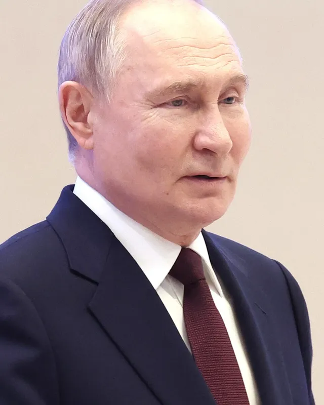 Photograph of Vladimir Putin in a dark suit, seated.